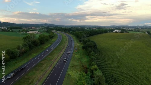 Aerial of cars, trucks, traffic driving fast on two lane divided highway, dramatic summer sky in green rural farm land countryside in USA America United States