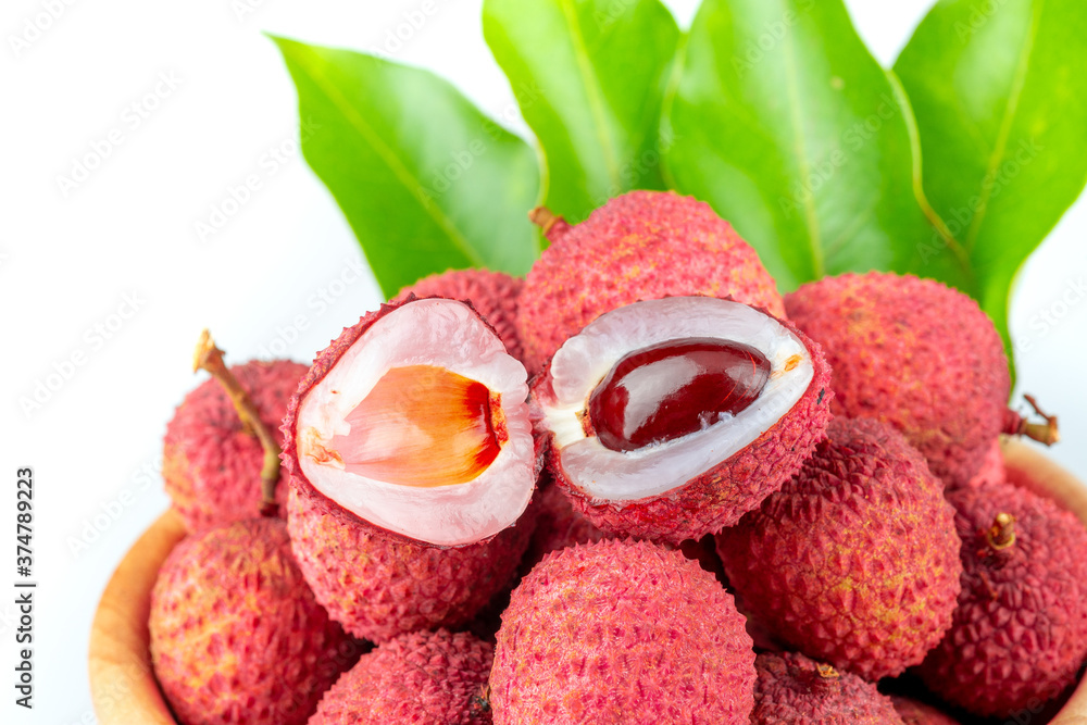 Lychee Hong Hui in a wooden bowl with branches and green leaves on a white background Lychee Hong Hui in a wooden bowl with branches and green leaves on a white background