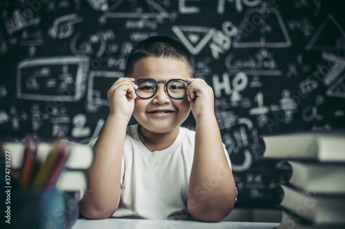 Boy studying and holding glasses leg in classroom.