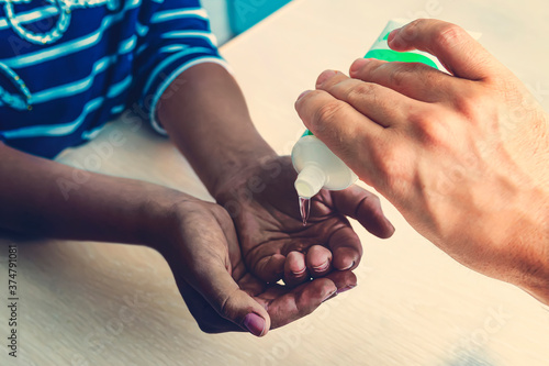 Protection from covid 19. Sanitizer hands. A European pours disinfection gel on the hands of a black girl at home. Caring for people during the coronavirus pandemic.