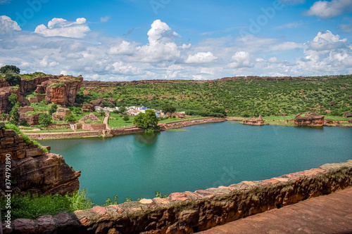 Landscape view of green Agastya lake of badami, with beautiful skies and mountains in the background.