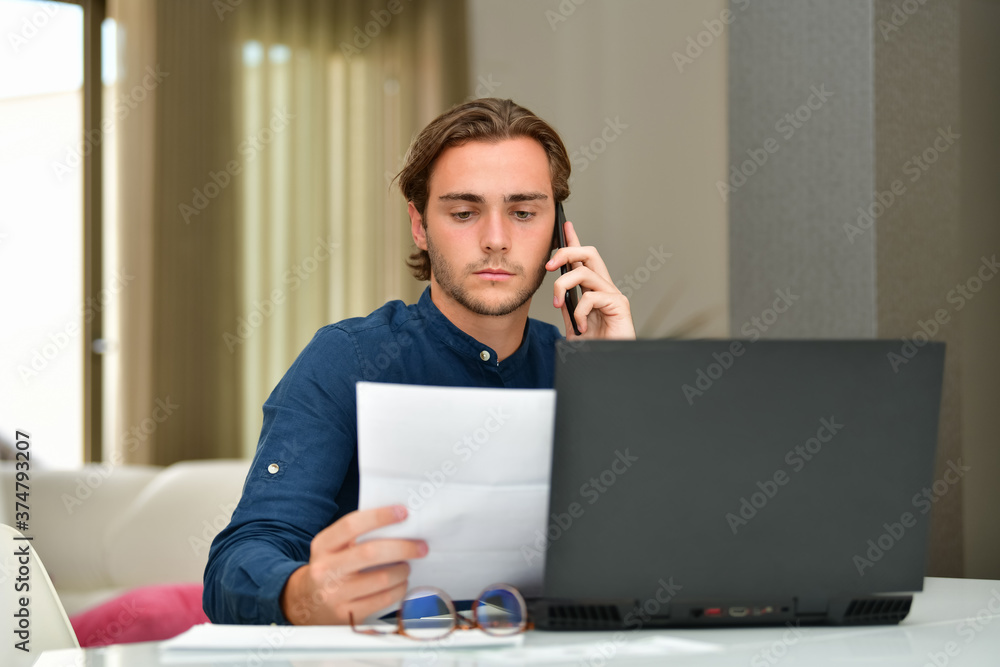 young man checking a bill while using his phone in front of a laptop on an out of focus background. Payments and technology concept. young man checking a bill while using his phone in front of a laptop on an out of focus background. Payments and technology concept.