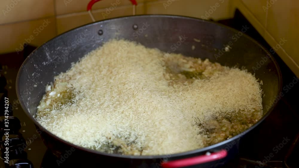 Putting rice in the pan with the sauteed seasoning to prepare paella Putting rice in the pan with the sauteed seasoning to prepare paella