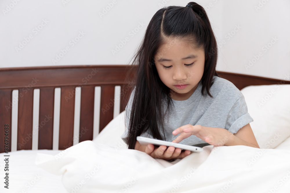 Asian little girl smiling in hands holding and play tablet on bed in bedroom. Little girl enjoy with tablet on bed. Asian girl looking and play tablet. Asian little girl smiling in hands holding and play tablet on bed in bedroom. Little girl enjoy with tablet on bed. Asian girl looking and play tablet.