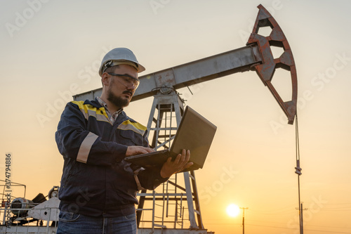 Engineer with a laptop against the background of oil rockers.