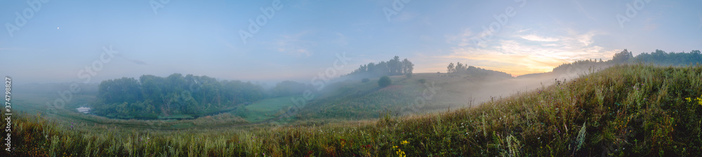 Beautiful summer hazy landscape with foggy valley and green hills before the sunrise.