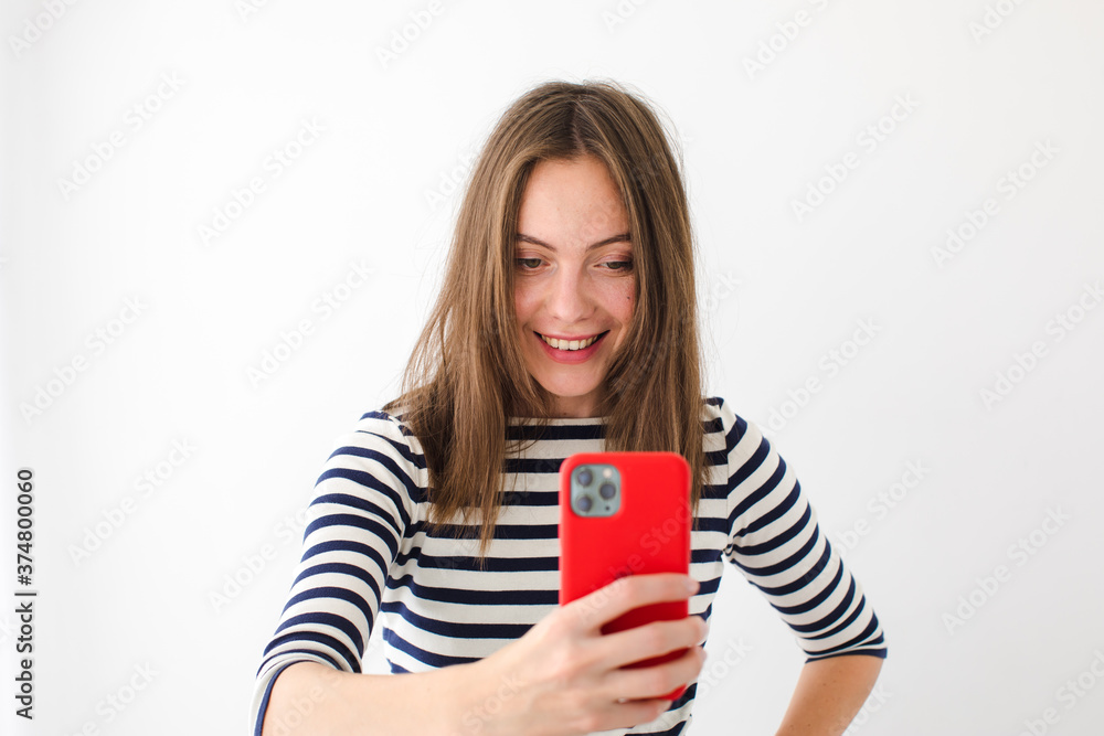 Smiling cute woman in a vest makes a photo on a red smartphone while standing on a white background Smiling cute woman in a vest makes a photo on a red smartphone while standing on a white background