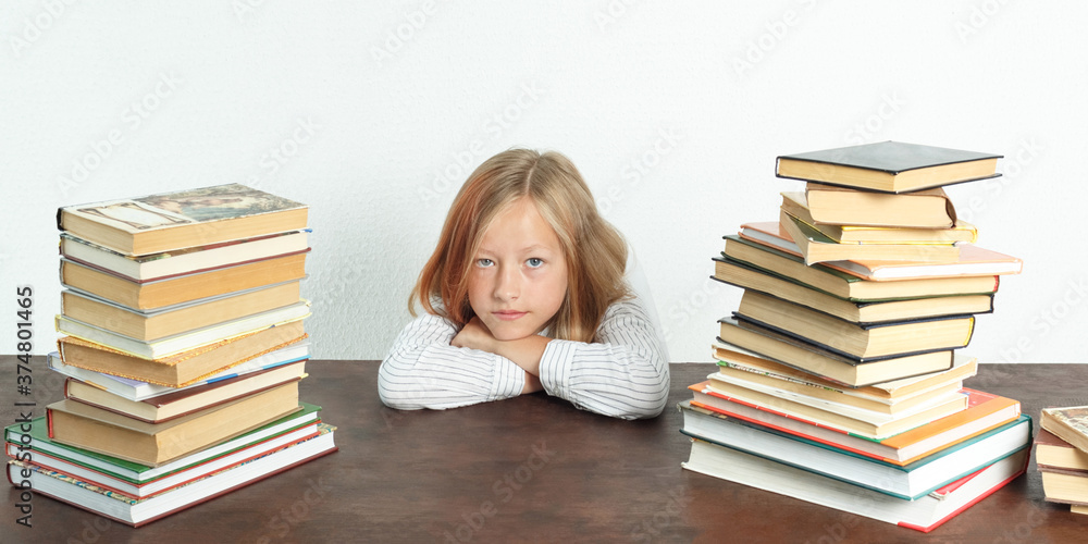 Portrait of a teenage girl who sits at a table among the books. Looks into the camera. Isolated background. Portrait of a teenage girl who sits at a table among the books. Looks into the camera. Isolated background.