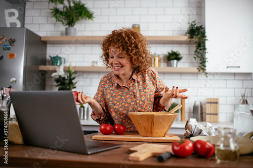 Young woman is reading a recipe while cooking. Beautiful woman with curly hair enjoying in the kitchen.