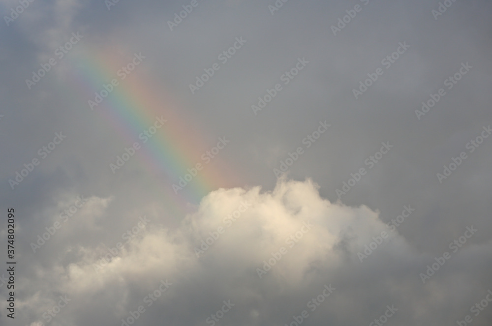 A short rainbow high in the dark clouds