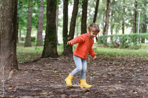 a little girl in a red sweater and yellow rubber boots runs through the park in early autumn. © Елена Гурова