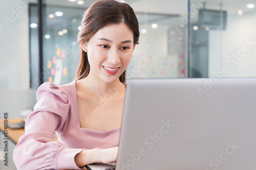 portrait of young beautiful asian business woman in casual pink t-shirt in the office,typing on laptop,Smile and have fun at work,Charming modern secretary female with a cheerful while working.