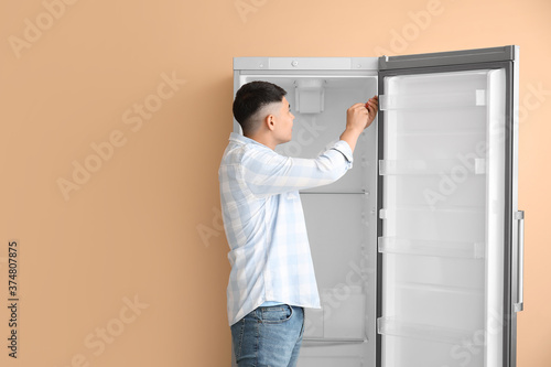 Worker repairing fridge on color background
