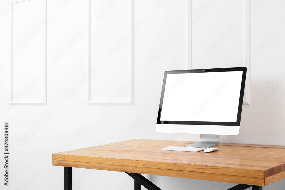 Modern PC monitor on table near light wall Modern PC monitor on table near light wall