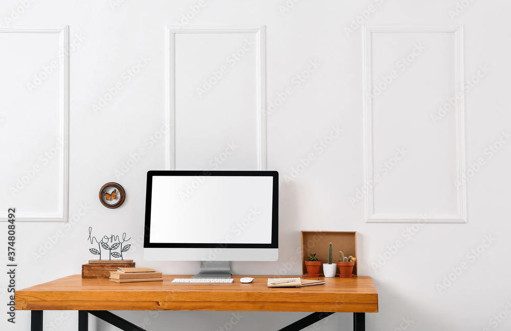 Modern PC monitor on table near light wall Modern PC monitor on table near light wall