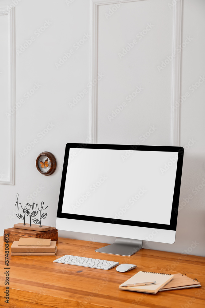 Modern PC monitor on table near light wall Modern PC monitor on table near light wall