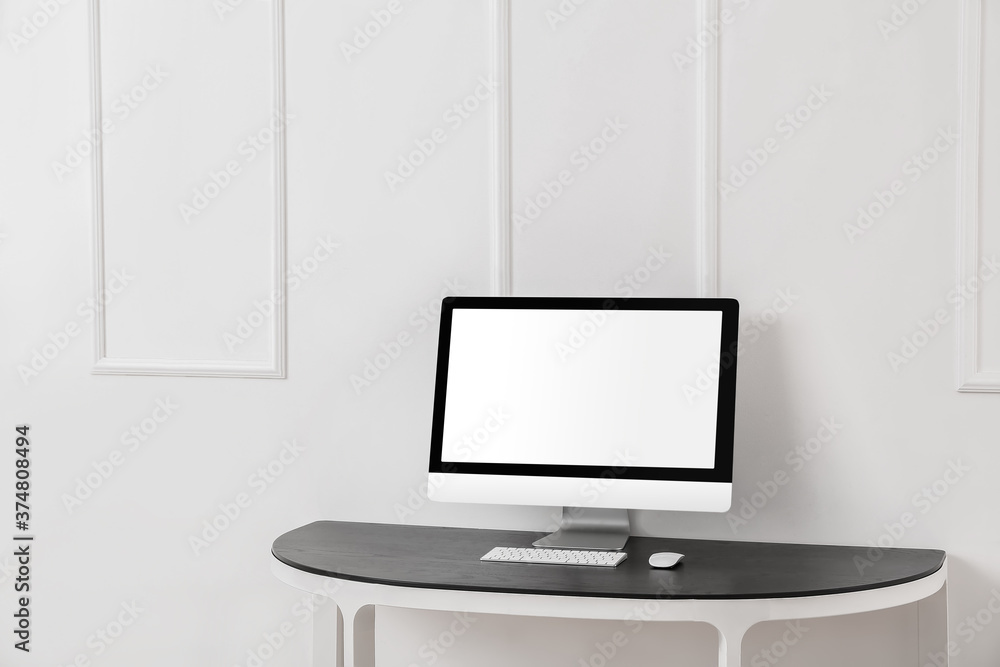 Modern PC monitor on table near light wall Modern PC monitor on table near light wall