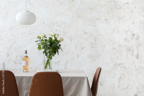 Dining table with wine and bouquet of flowers near light wall photo