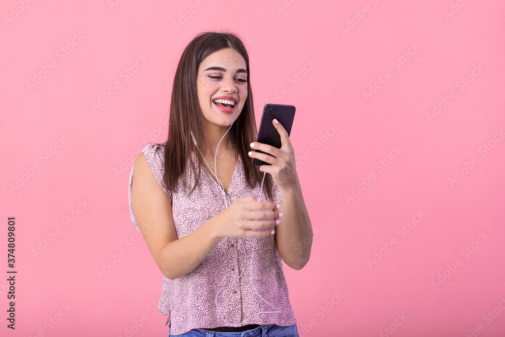 Excited beautiful girl hold mobile phone with headphones listening to music on blank empty screen isolated on pink studio background . Emotions, lifestyle concept. Copy space. Excited beautiful girl hold mobile phone with headphones listening to music on blank empty screen isolated on pink studio background . Emotions, lifestyle concept. Copy space.