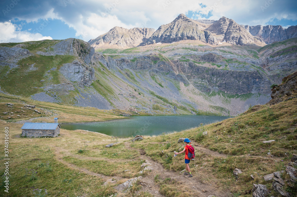 Fototapeta premium boy with hat and backpack walks by the lake sabocos in the mountains of the pyrenees, on a path