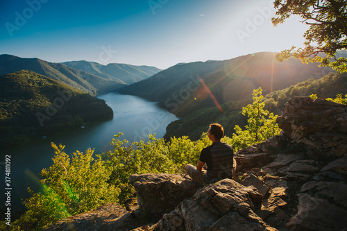 Fotografie Traveler enjoying sunset on a cliff with a beautiful view of a lake