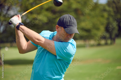 Male golfer swinging at the ball with a driver as he takes his shot on a golf course in a closeup upper body view in a healthy active lifestyle concept