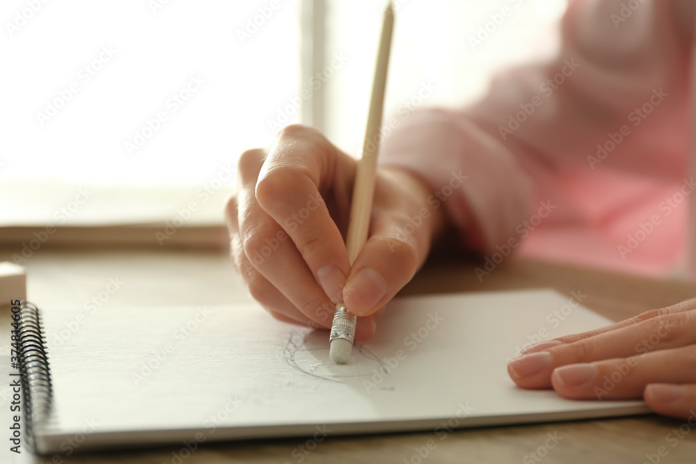 Woman correcting picture in notepad with pencil eraser at wooden table, closeup Woman correcting picture in notepad with pencil eraser at wooden table, closeup