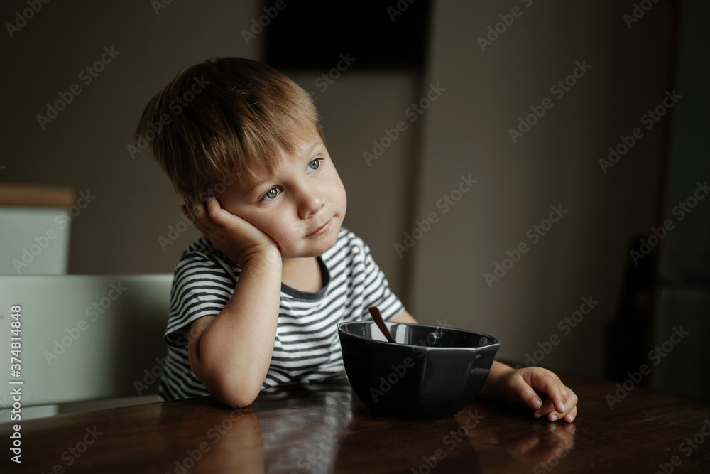 cute little boy eating oatmeals for beakfast dreamily looking at the window. image with selective focus cute little boy eating oatmeals for beakfast dreamily looking at the window. image with selective focus