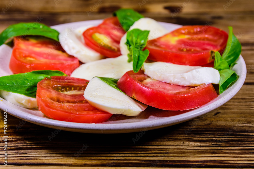 Plate with caprese salad (italian salad with cherry tomatoes, mozzarella cheese and basil leaves) on wooden table