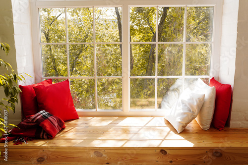 Fotografie Forest with autumn colors seen through a window , windowsill with red and white