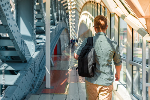 A young man in sunglasses and a shirt walks along a modern glass business corridor