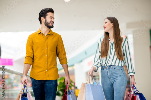 Portrait of cheerful friends spouses man woman have free time in shopping mall go walk hold many packages purchase wear yellow striped shirt denim jeans