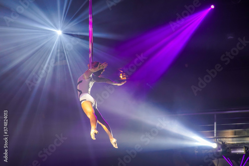 Flexible young woman make performance on aerial straps, flexible back on aerial straps, aerial circus show, purple white light. Flexible woman gymnast on straps