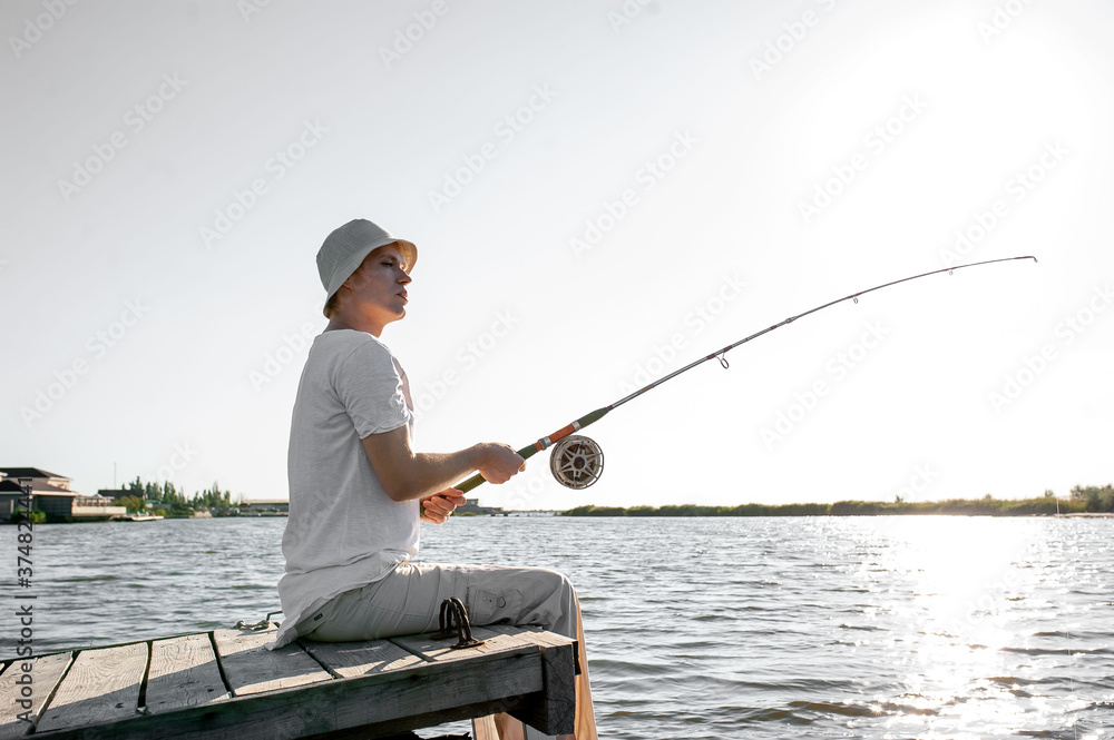 a young fisherman sits on the bridge with a fishing rod and catches fish a young fisherman sits on the bridge with a fishing rod and catches fish