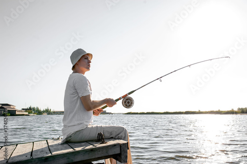 a young fisherman sits on the bridge with a fishing rod and catches fish