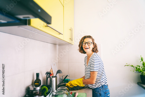 Beautiful happy young woman washing dishes in the sink at home in yellow gloves, cleaning the house