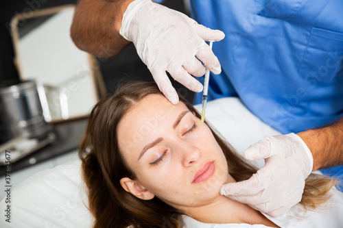Young female patient receiving injections for face skin tightening in cosmetology clinic .