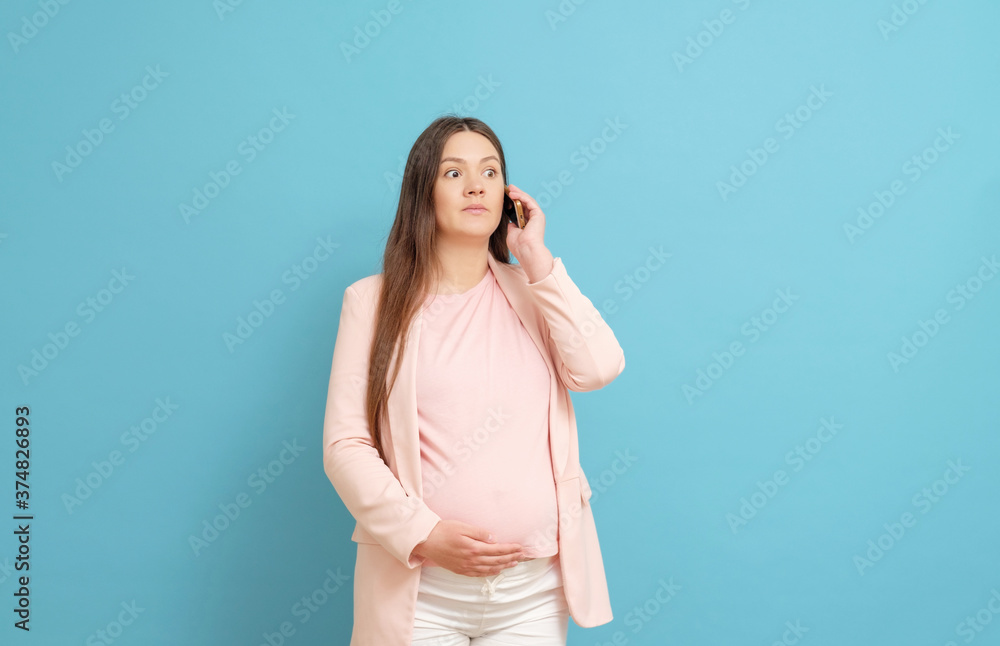 frightened young pregnant woman on blue background calls by mobile phone, discharge of amniotic fluid, the beginning of labor process frightened young pregnant woman on blue background calls by mobile phone, discharge of amniotic fluid, the beginning of labor process