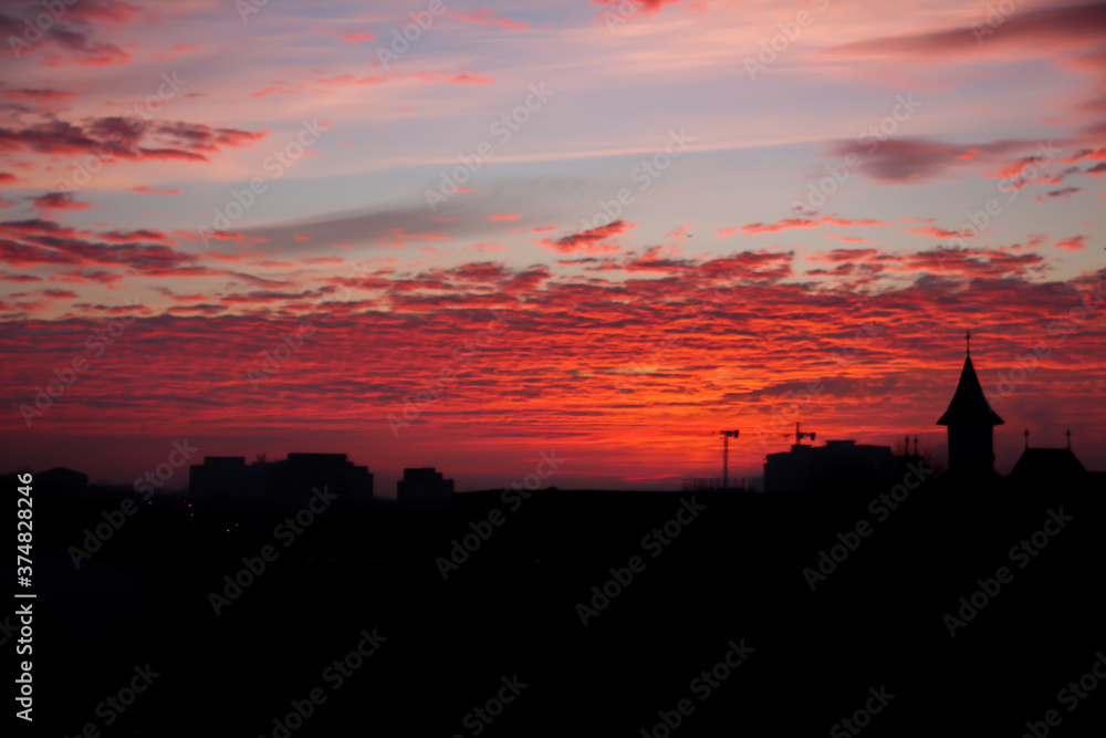 Red sky full of orange clouds during a morning sunrise with silhouette buildings
