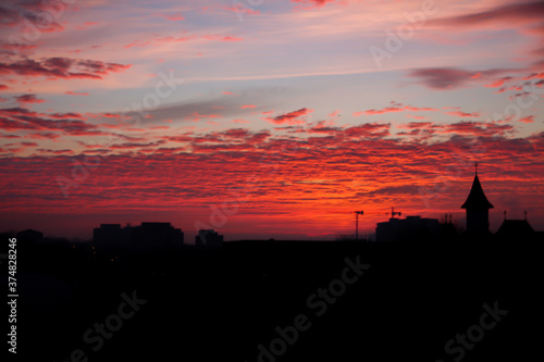 Red sky full of orange clouds during a morning sunrise with silhouette buildings © Codrin Rusu
