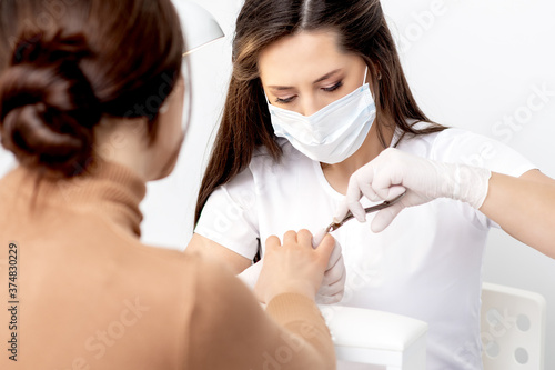 Manicurist in protective mask using manicure cutter to remove cuticle of female nails in manicure salon