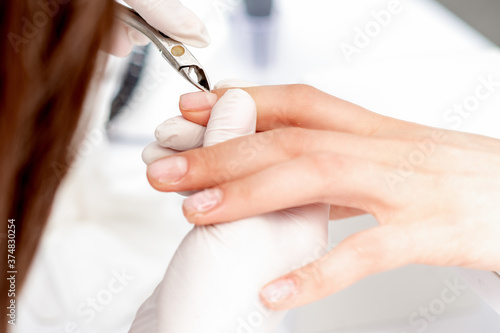 Close up of manicurist using manicure clipper to remove cuticle of female nails in manicure salon