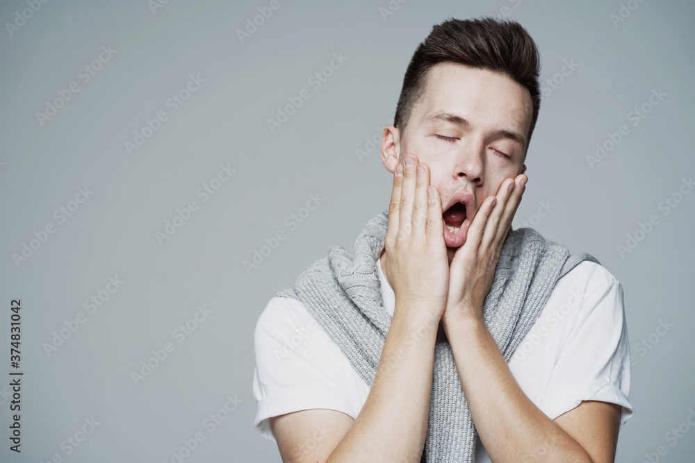 yawns tired of work hands touch the face of a young man of European appearance, thinks what to do how to help yourself. eyes closed, mouth open yawns tired of work hands touch the face of a young man of European appearance, thinks what to do how to help yourself. eyes closed, mouth open