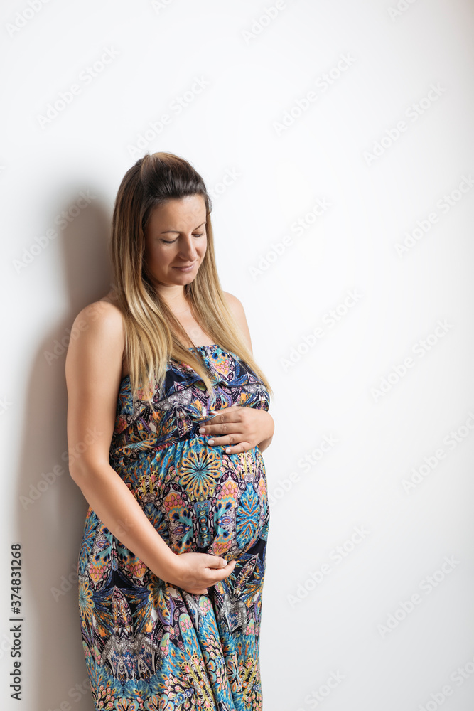Beautiful pregnant woman in colorful dress on white background. Her arms are all around belly. Beautiful pregnant woman in colorful dress on white background. Her arms are all around belly.