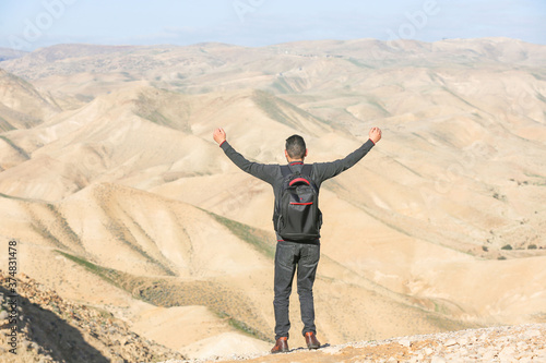 A young man stands on a hill and looks at the mountains