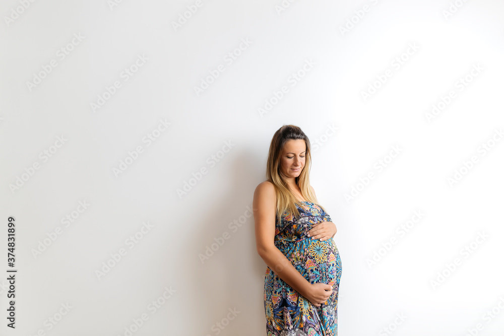 Beautiful pregnant woman in colorful dress on white background. Her arms are all around belly. Beautiful pregnant woman in colorful dress on white background. Her arms are all around belly.