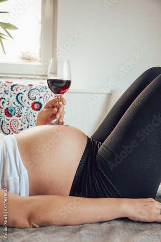 Pregnant woman holding a glass of wine on her belly. © Kitja