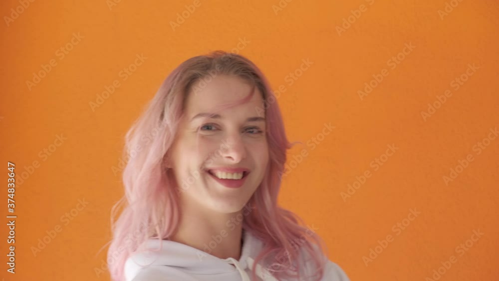 A young beautiful woman is spinning in one place. Looks into the camera. Human emotions. Orange background. A young beautiful woman is spinning in one place. Looks into the camera. Human emotions. Orange background.
