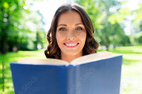 leisure and people concept - happy smiling young woman reading book at summer park