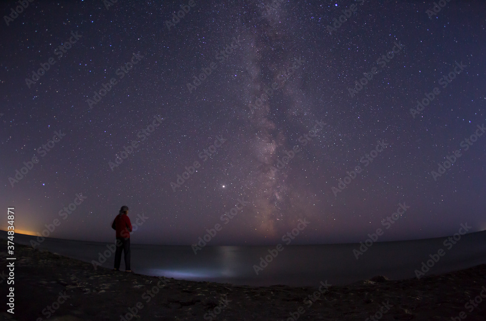 A man stands by the sea and looks at the milky way in a starry night A man stands by the sea and looks at the milky way in a starry night